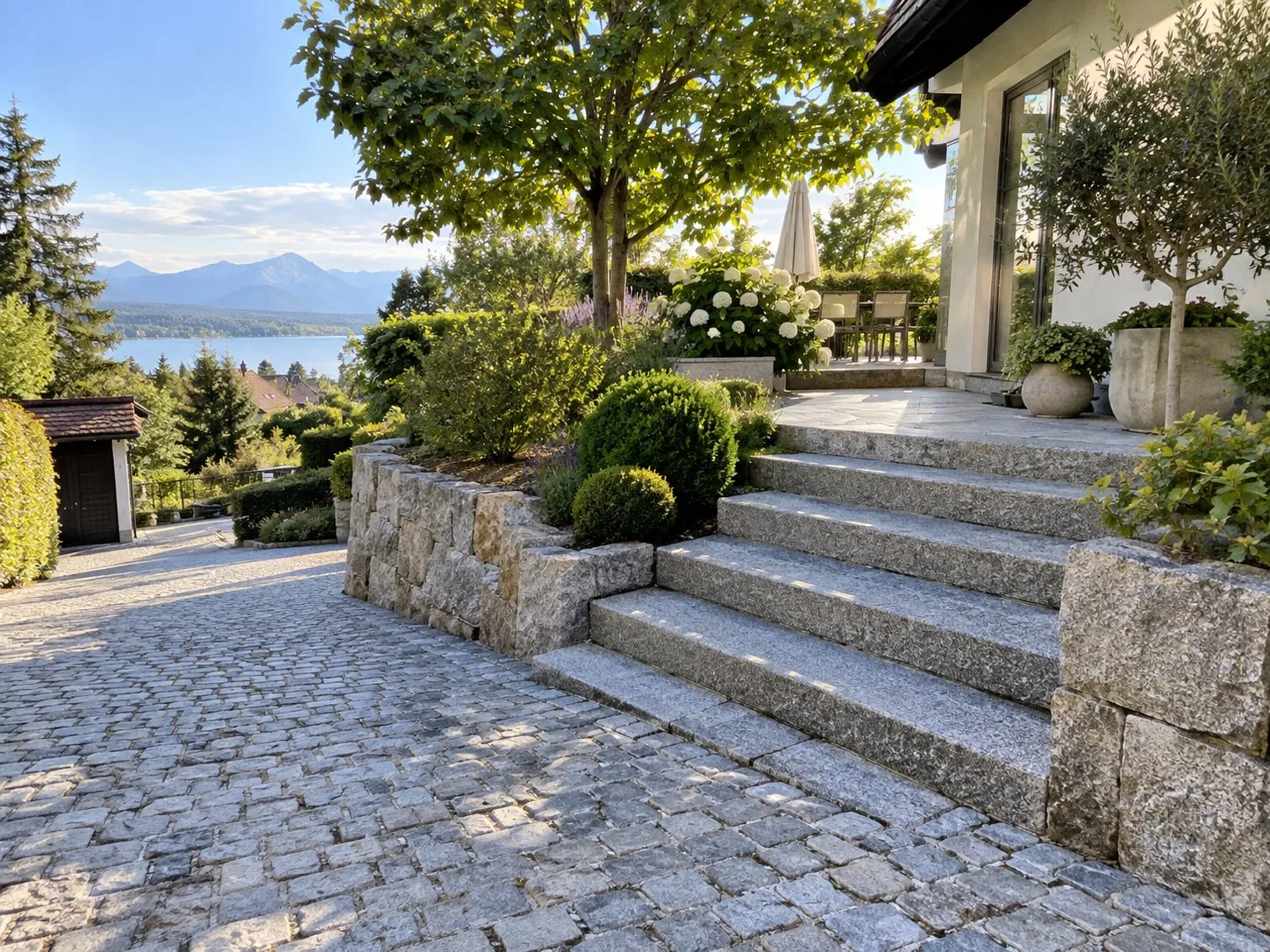 Breite Granitstufen zu einer Terrasse neben einer Einfahrt aus Granitpflaster